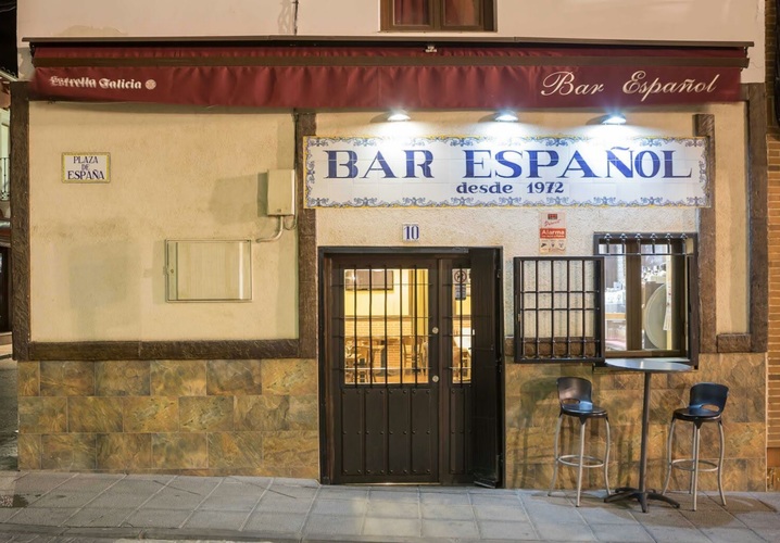 Fachada del Bar Español de noche, con el cartel de azulejos iluminado sobre la puerta